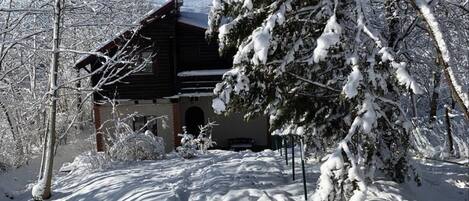 A snow-covered cabin with a satellite dish, surrounded by trees and snow.
