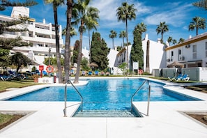 A swimming pool with lounge chairs, palm trees, and white buildings.