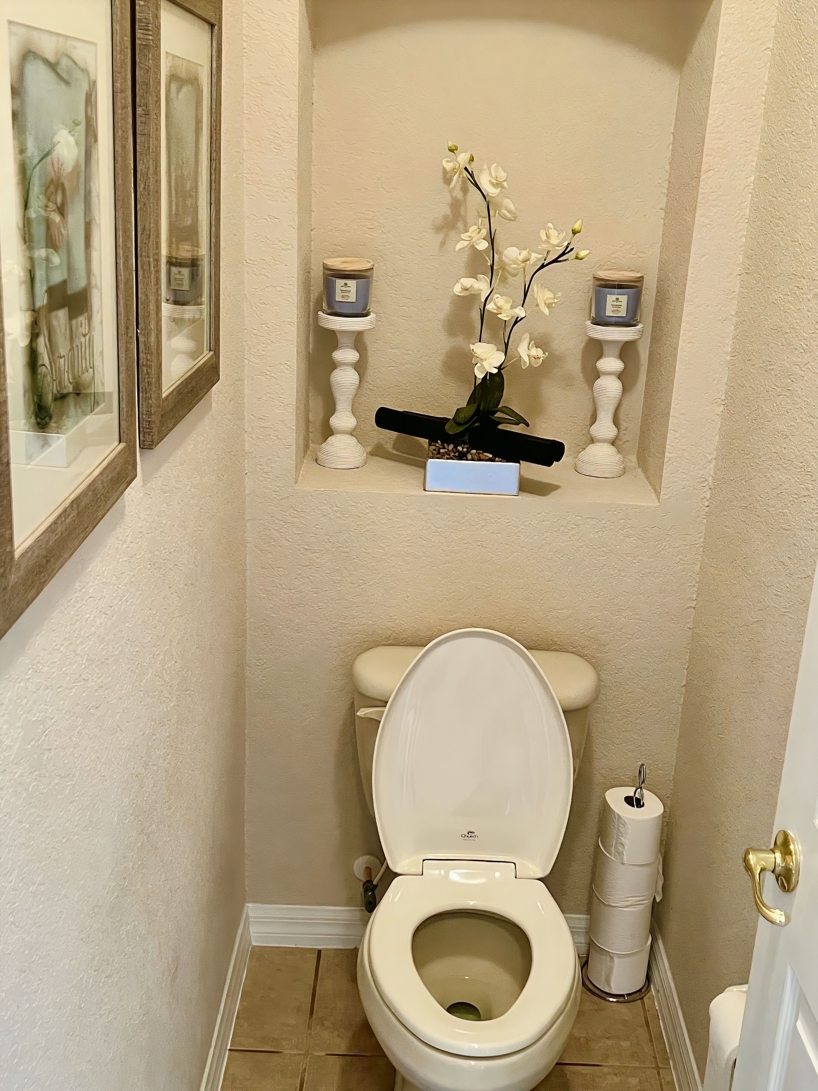 A bathroom with a toilet, a shelf with two candles, and a framed picture on the wall.
