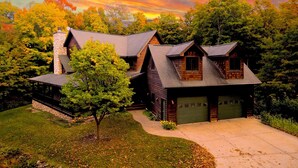 A modern two-story house with a stone chimney, a covered front porch, and a garage.
