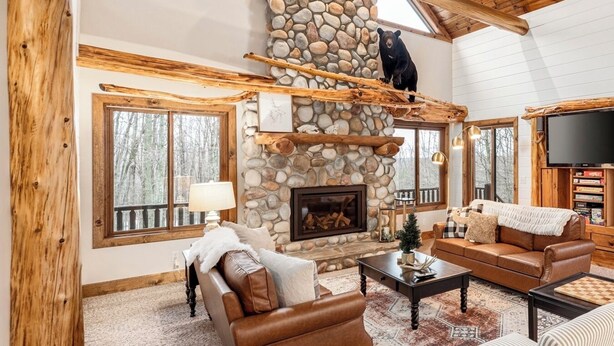 A spacious living room with a stone fireplace, wooden beams, and a bear sculpture.