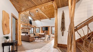 A spacious living room with a stone fireplace, wooden beams, and a large window.