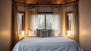 A large bed with a white duvet, two bedside lamps, and a window with curtains.