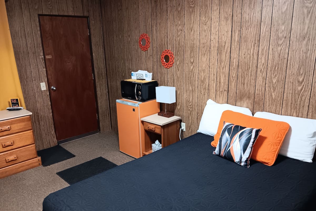Ett hotellrum med en säng, ett skrivbord, en mikrovågsugn, en lampa och en garderob.