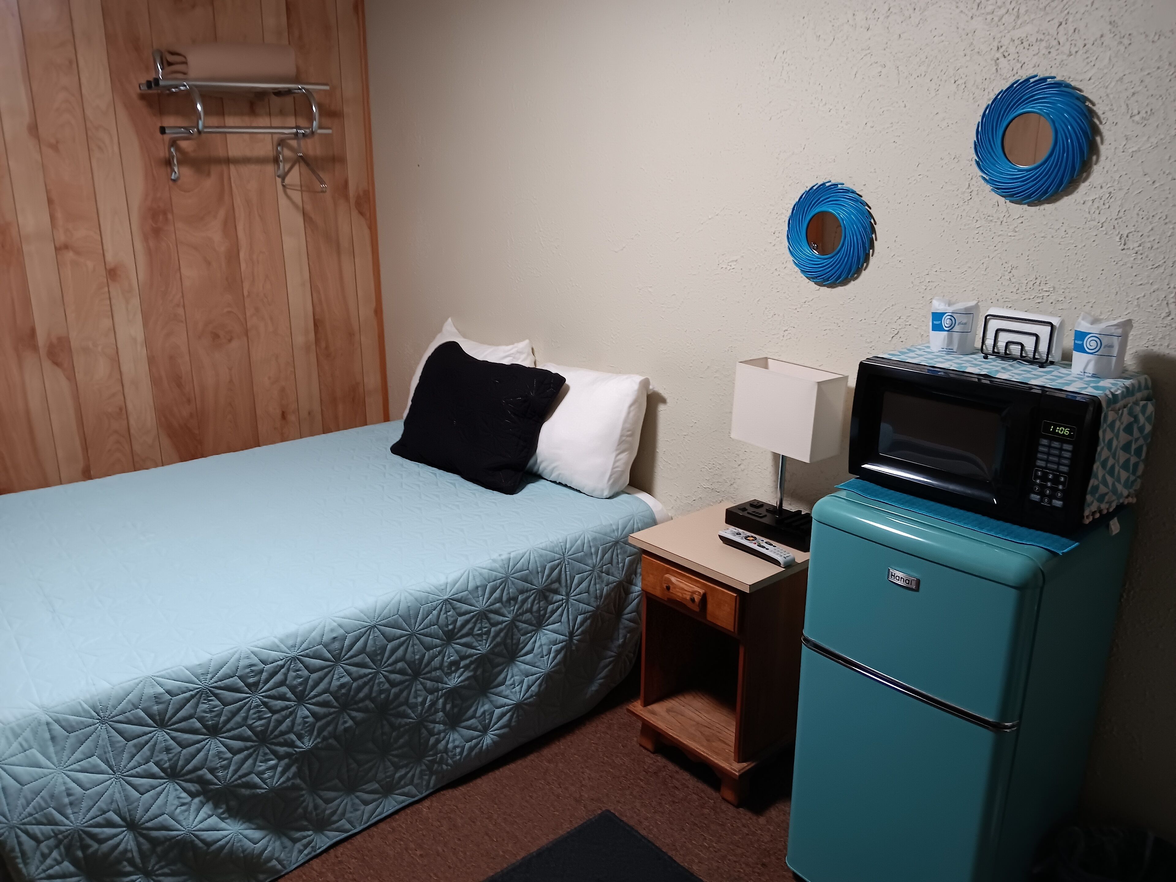 A hotel room with a bed, a nightstand, a microwave, and a small cabinet.
