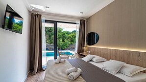 Una habitación de hotel moderna con una cama grande, un televisor de pantalla plana, un cabecero de madera y vistas a una piscina al aire libre.