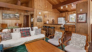 A cozy cabin interior with a wooden dining table, a sofa, and a kitchen area.