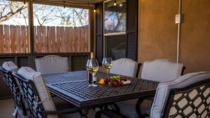 A patio with a table and chairs, a bottle of wine, and a fruit platter. - The Werken Haus | Pool | Pet-friendly | 2 Blks to Main (Fredericksburg)