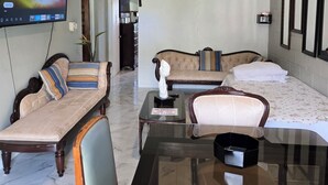A hotel room with a TV, ceiling fan, two beds, a sofa, and a dining table. - Sweets Beach View in the heart of  Ocho Rios (Ocho Rios)