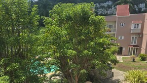 A balcony with a view of a landscaped garden, a building with a red roof, and a mountain in the background. - Sweets Beach View in the heart of  Ocho Rios (Ocho Rios)