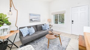 Una sala moderna con un sofá gris, almohadones azules estampados, una mesa de centro de madera y una lámpara colgante.