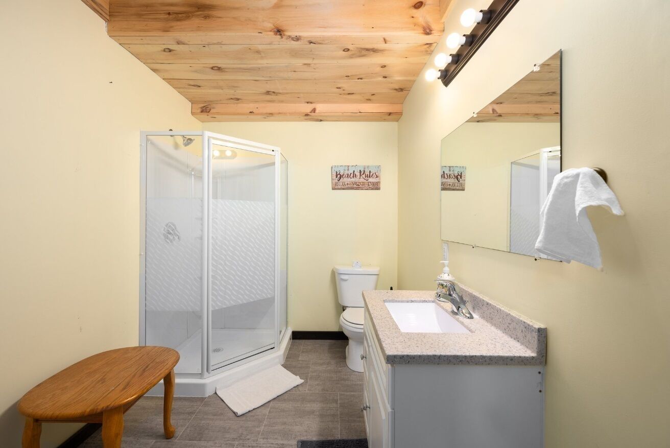 A bathroom with a shower, toilet, sink, and wooden bench.