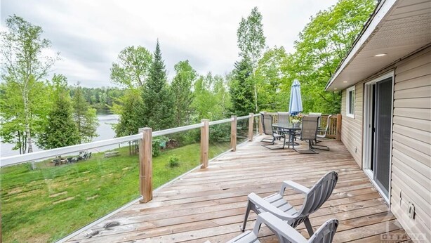 Une terrasse en bois, agréée de mobilier d’extérieur, qui offre une vue sur un lac et est entourée d’arbres.