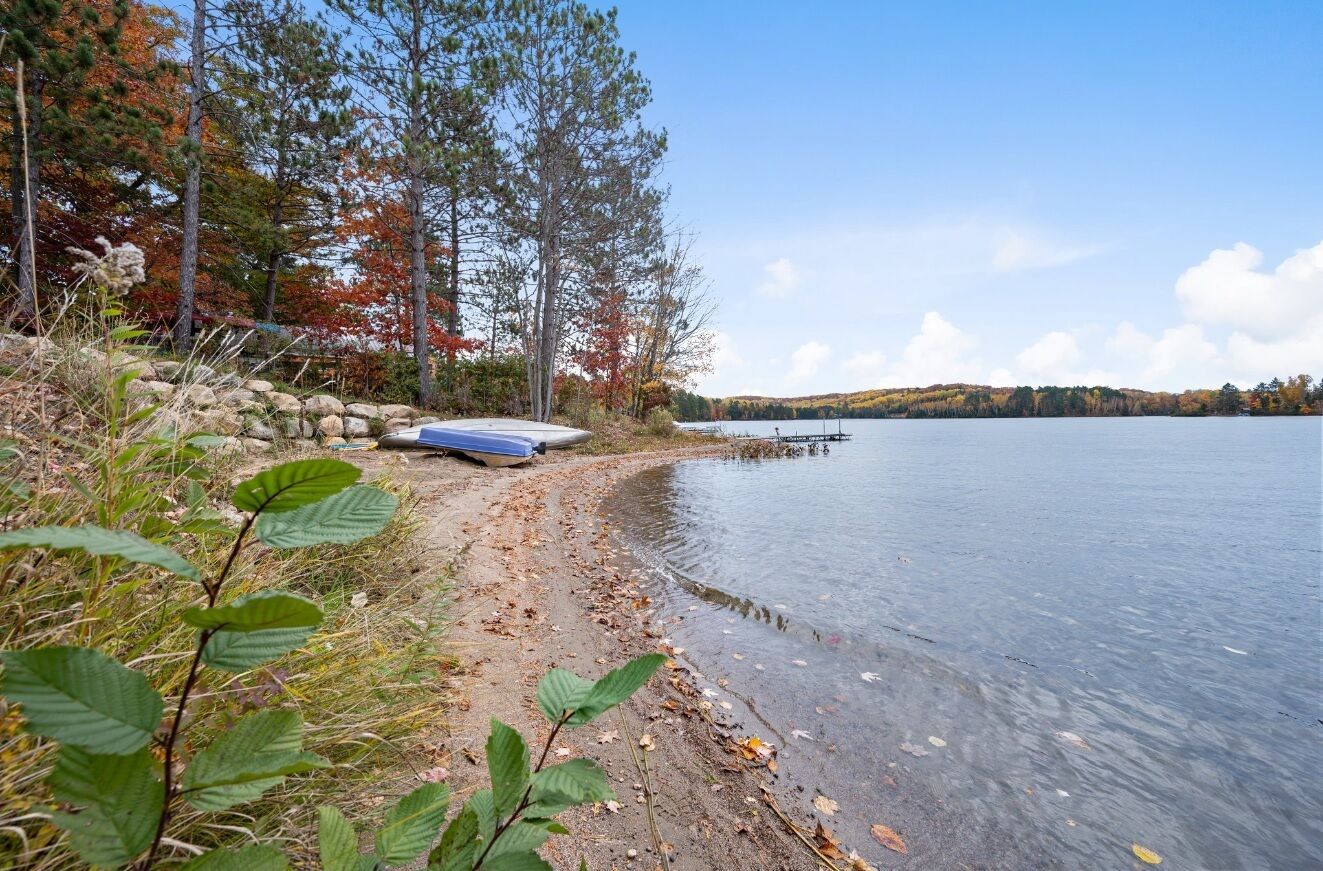 A lakeside scene with a dock, boats, and autumn foliage.