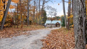 Une cabane accessible par un sentier de terre, entourée d’arbres aux feuilles d’automne.
