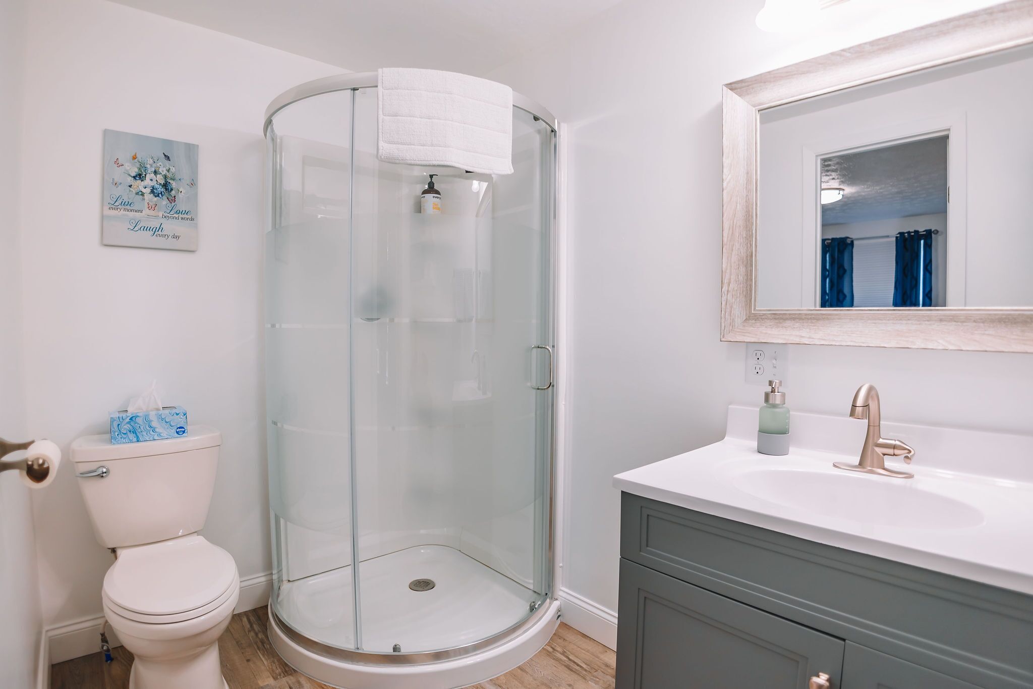 Une salle de bain dotée d’une douche à parois de verre, de toilettes blanches, d’un lavabo avec un robinet doré et d’un miroir au-dessus du lavabo.
