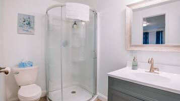 Une salle de bain dotée d’une douche à parois de verre, de toilettes blanches, d’un lavabo avec un robinet doré et d’un miroir au-dessus du lavabo.