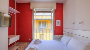 Quarto de hotel com cama, televisão, varanda e parede vermelha.