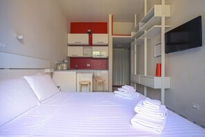 Een hotelkamer met een bed, een kitchenette, een televisie en een zithoekje.
