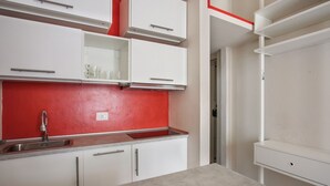 Cozinha com armários brancos, painel de fundo vermelho e pia de aço inoxidável.