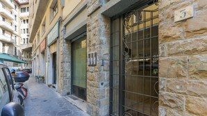 Rua estreita com edifícios de pedra, um portão de metal e scooters estacionadas.
