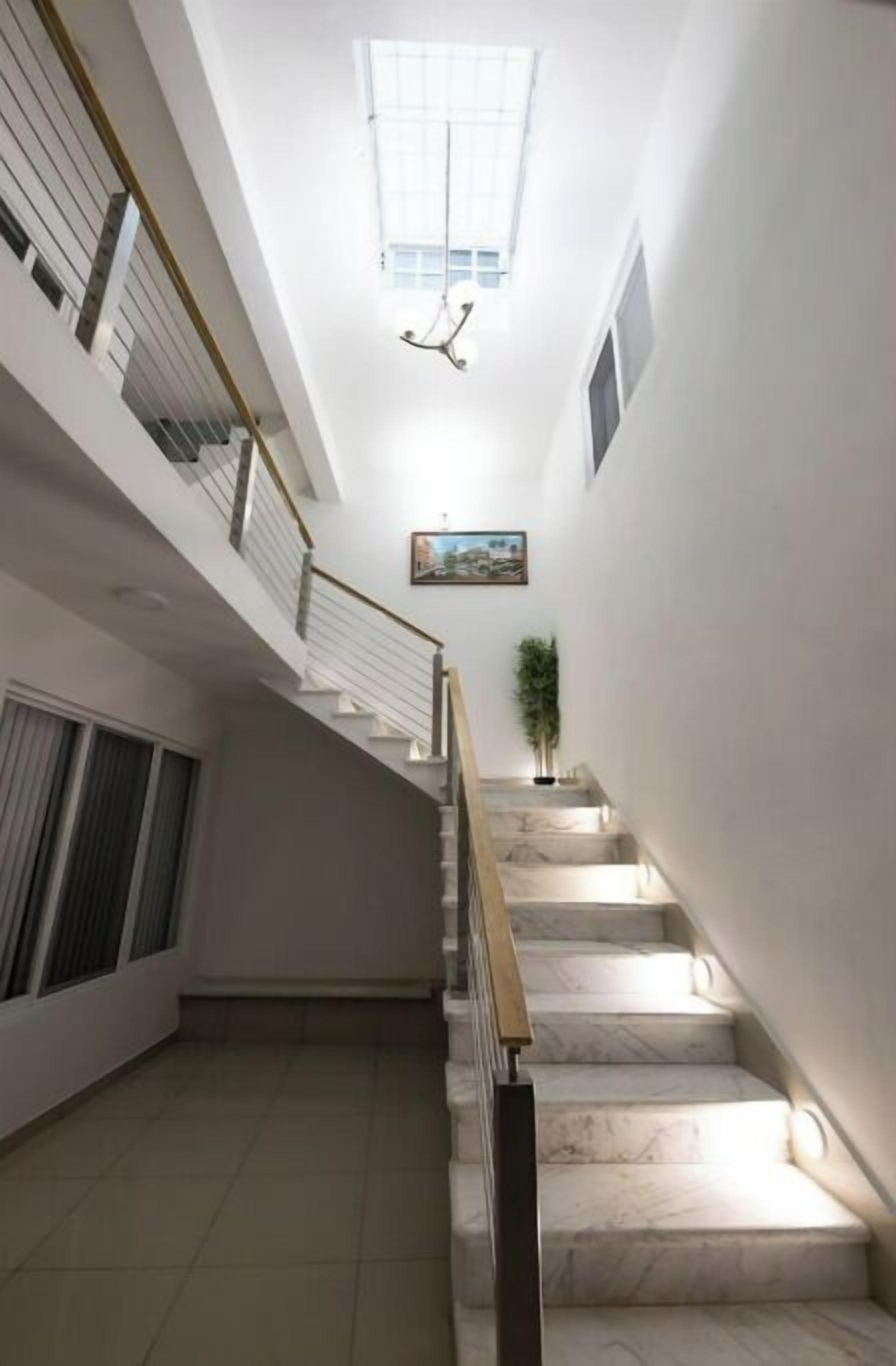 A staircase with marble steps and a handrail, leading to a landing with a window and a painting.