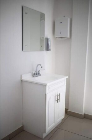 Bathroom features a vanity with a single faucet, two drawers, and a wall-mounted dispenser.