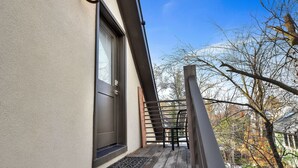 Una terraza de madera con barandal metálico, una puerta con ventana y un aplique de pared.