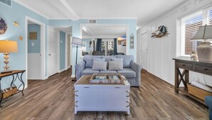 Een woonkamer met een blauwe bank, een witte salontafel en een houten vloer.