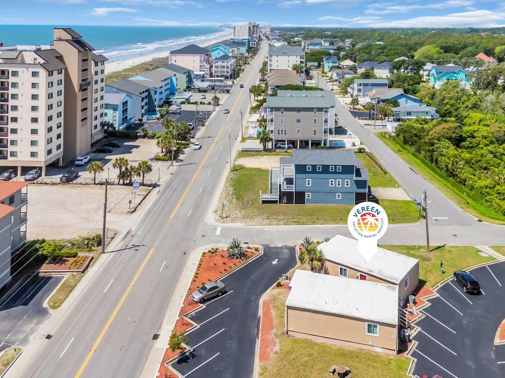 A coastal town with a mix of residential and commercial buildings, a main road, and a beach in the background.