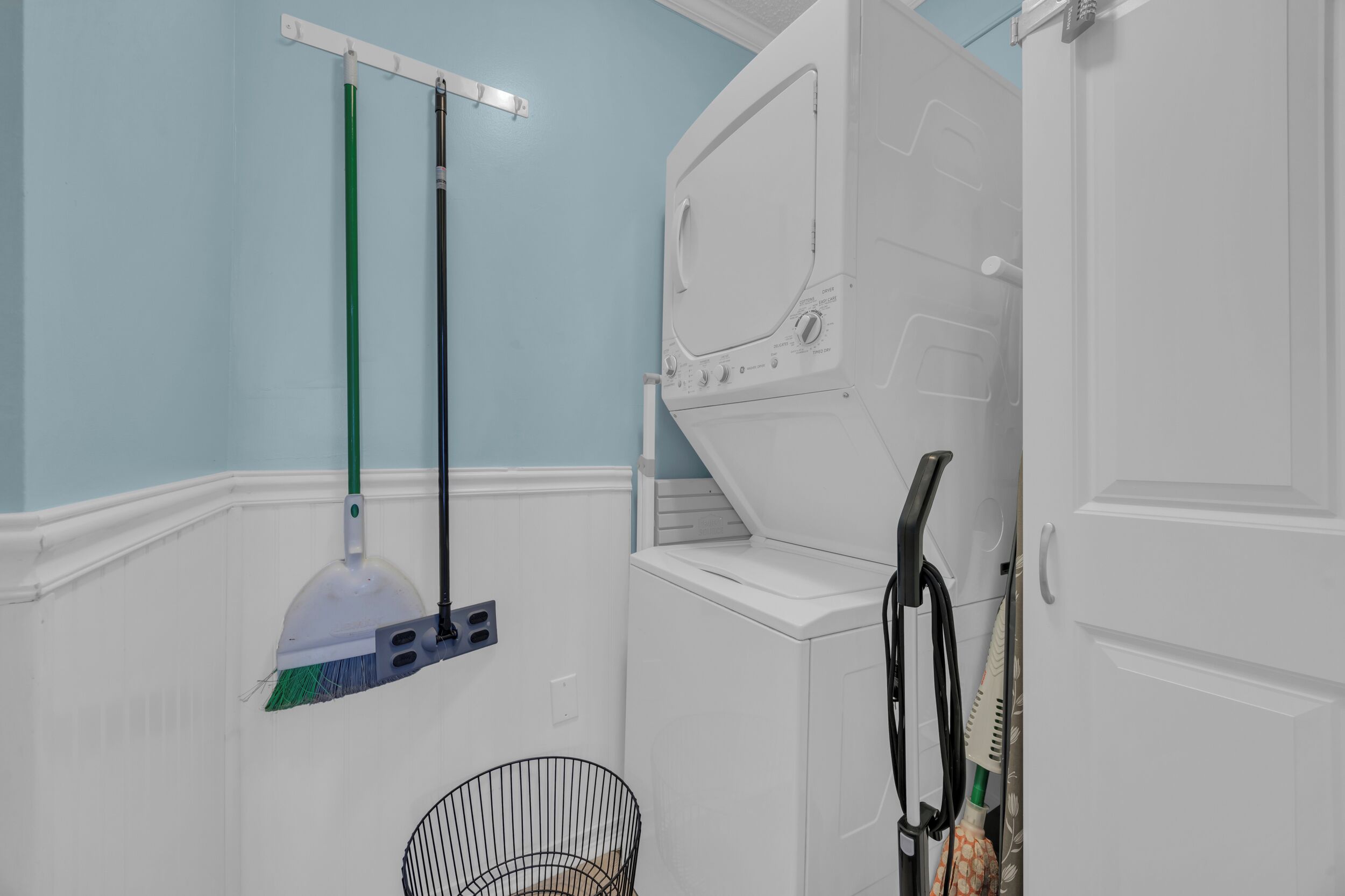 A laundry area with a washing machine, a broom, and a dustpan.