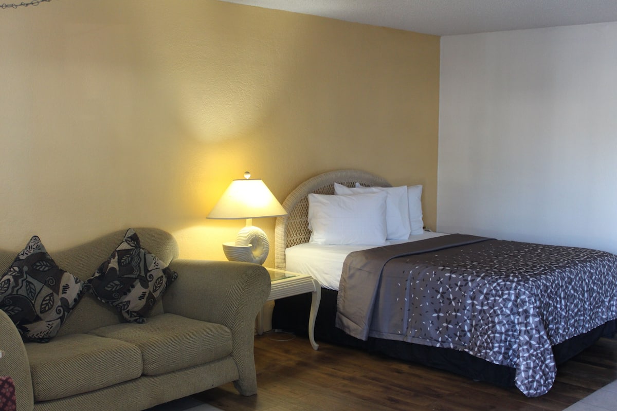 Une chambre d’hôtel comprenant un lit, un canapé, une table de chevet avec une lampe et un mur orné d’un motif texturé.