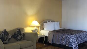 A hotel room with a bed, a sofa, a nightstand with a lamp, and a wall with a textured pattern.