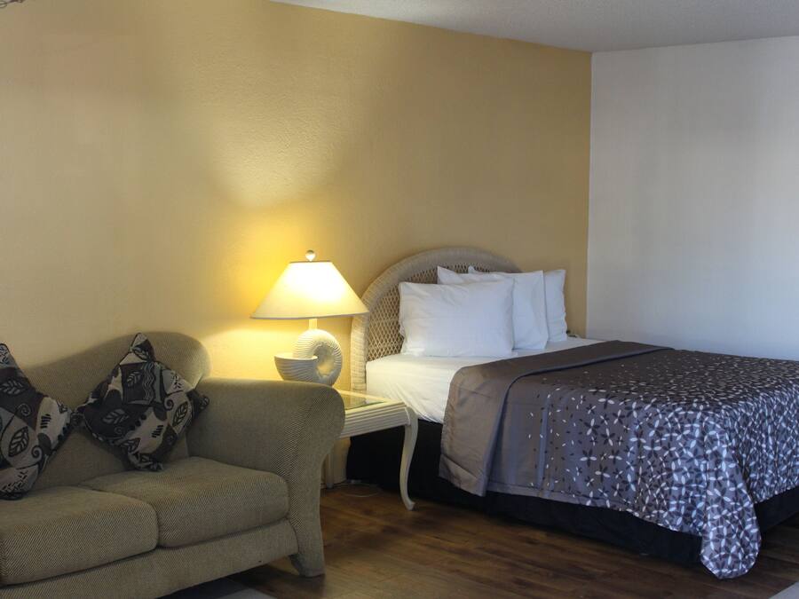 A hotel room with a bed, a sofa, a nightstand with a lamp, and a wall with a textured pattern.