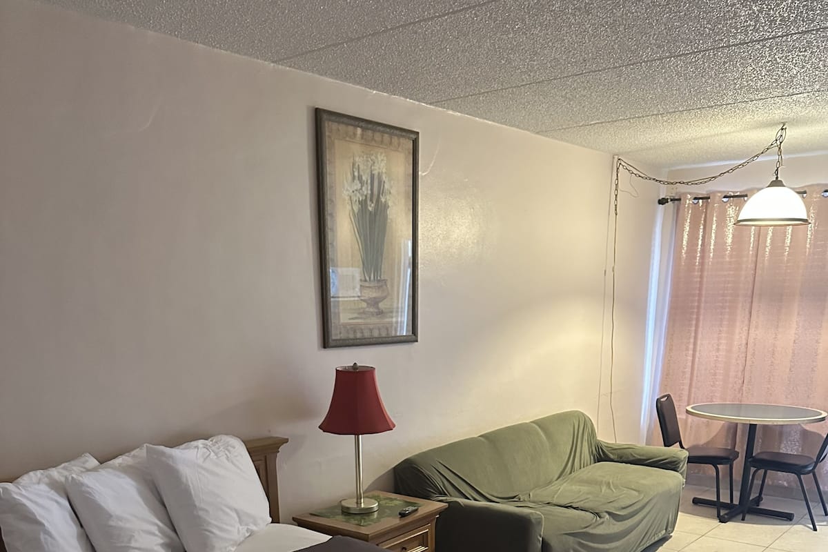 Une chambre d’hôtel avec un lit, un canapé vert, une table avec des chaises, une lampe et un tableau au mur.