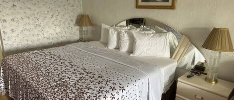 Un lit bien fait, recouvert d’une couvre-lit à motifs, une lampe de chevet, une table de chevet avec une lampe et un tableau encadré au mur.