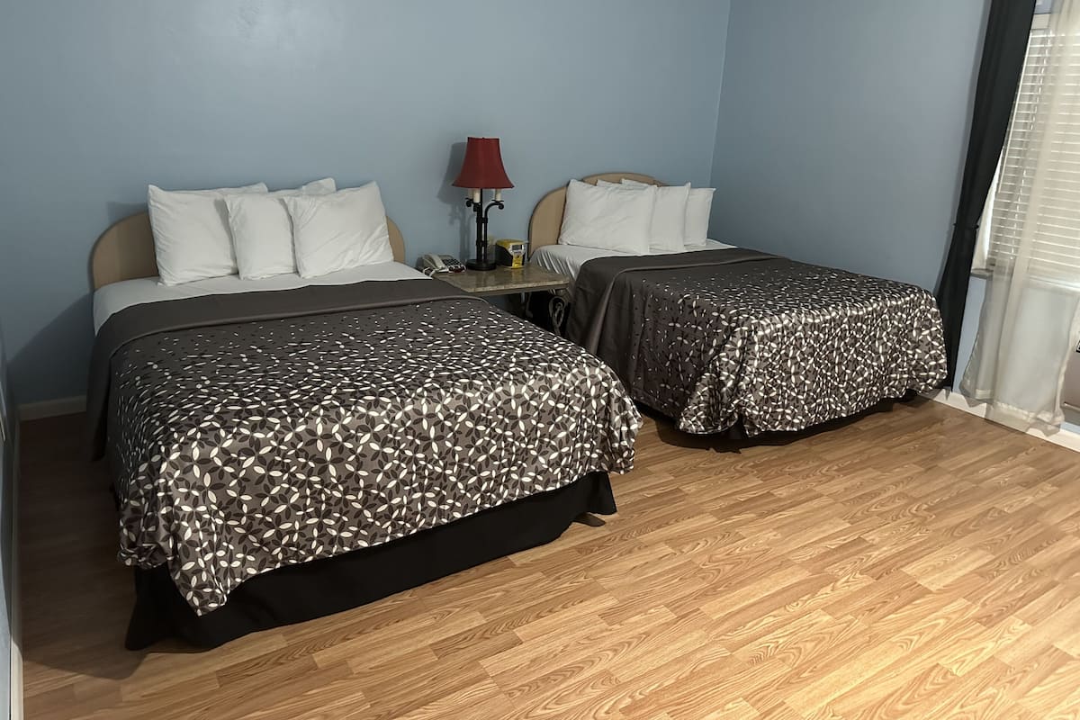 Une chambre d’hôtel avec deux lits, une table de chevet, une lampe et une fenêtre avec des stores.