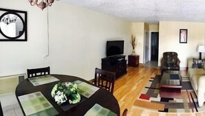 A compact living space with a dining area, a sofa, a television, and a kitchenette.