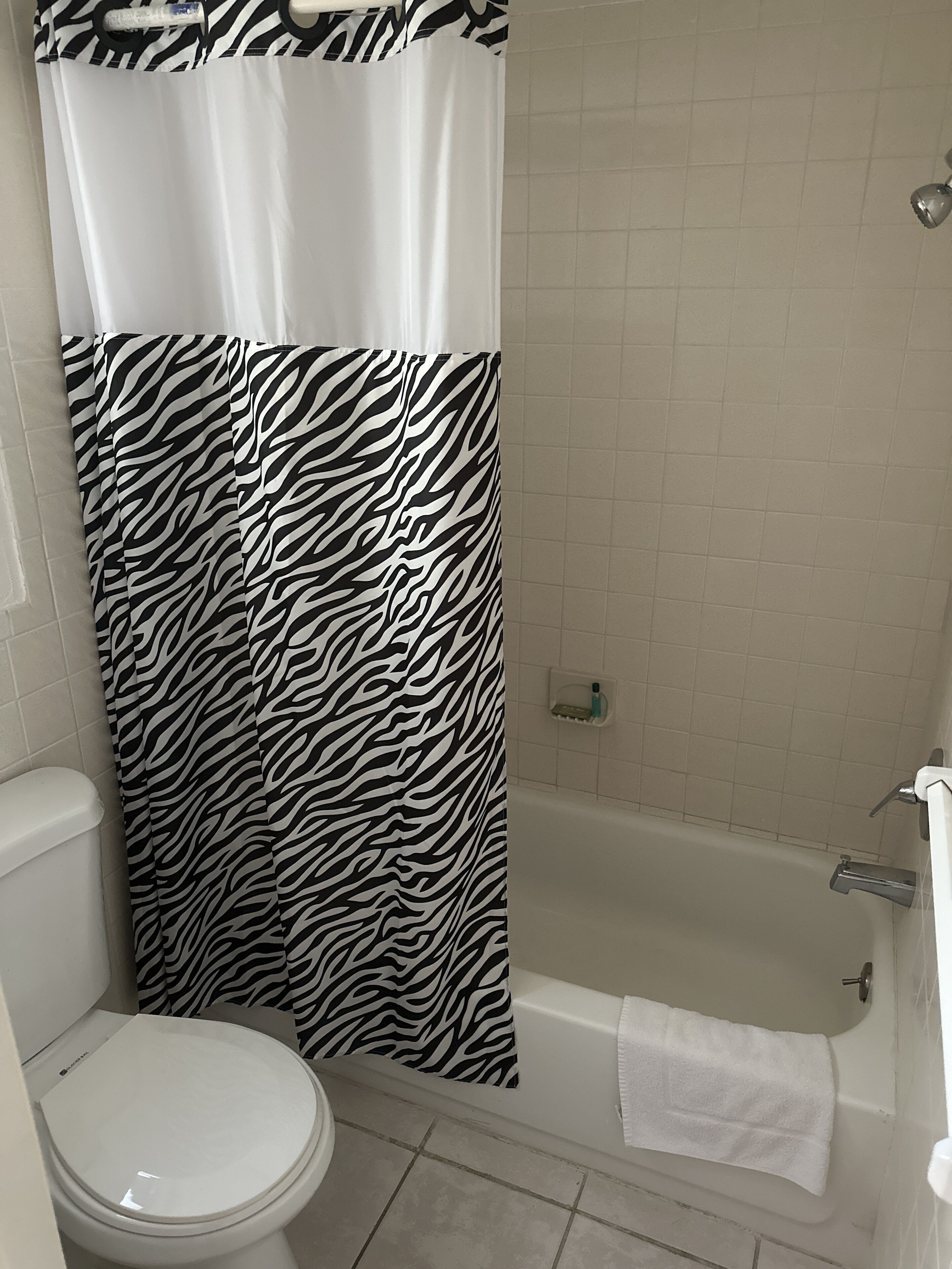 Une salle de bain avec un rideau de douche à motifs zébrés, des toilettes blanches et une baignoire avec une serviette blanche.