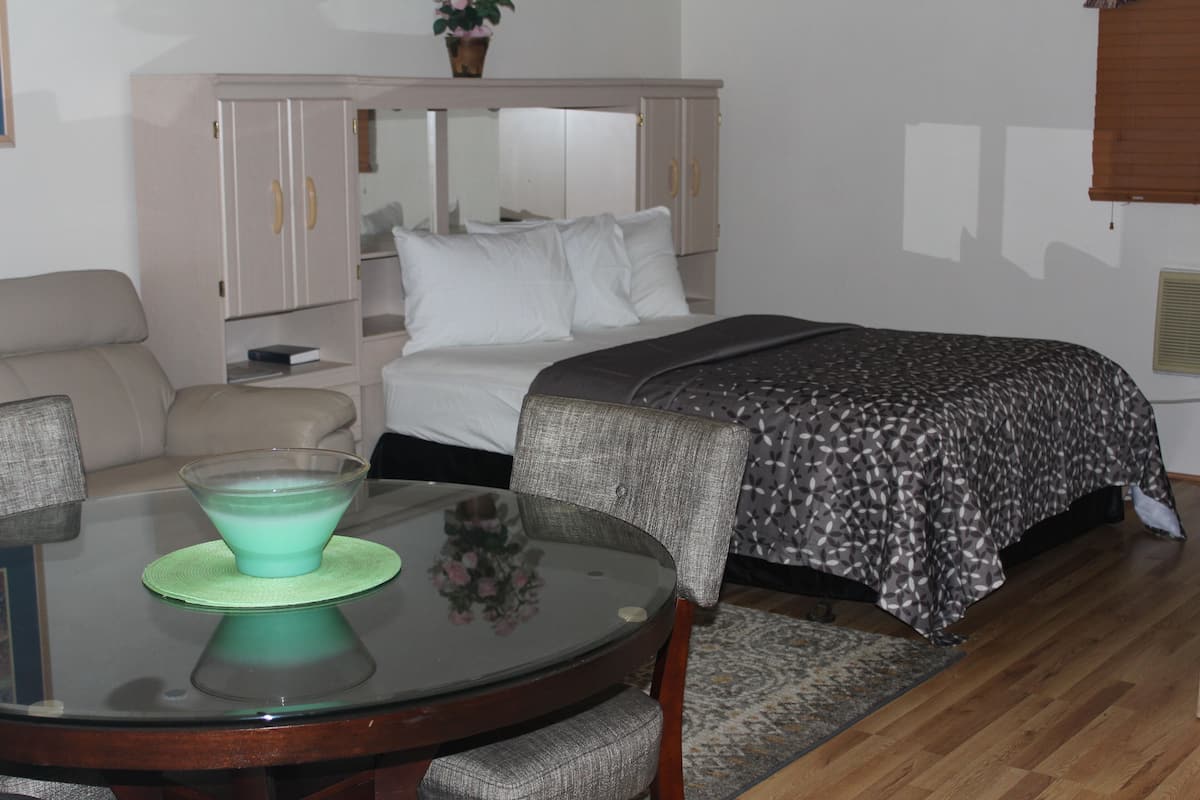 Une chambre à coucher comprenant un lit, une table de chevet, une commode, une table en verre avec un bol vert et une chaise.