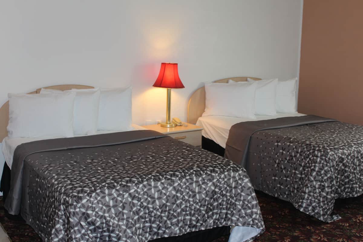 Une chambre d’hôtel avec deux lits, chacun recouvert d’une couvre-lit à motifs, dotée d’une lampe de chevet et d’une table de nuit.