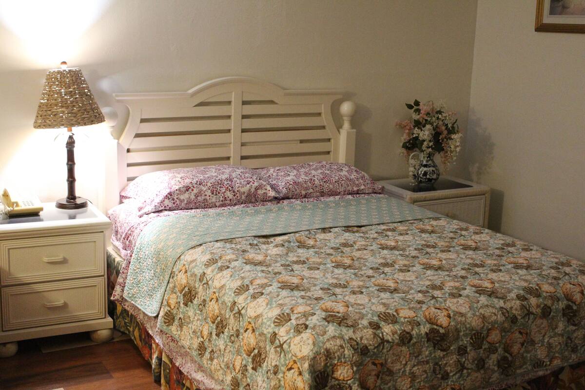 Une chambre à coucher comprenant un lit, une table de chevet avec une lampe, un vase avec des fleurs et une commode.