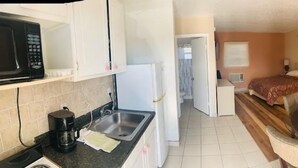 A compact hotel room with a kitchenette, a bed, a dining area, and a small sitting area.