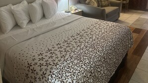 A hotel room with a bed, a chair, a small table, a lamp, and a painting on the wall.
