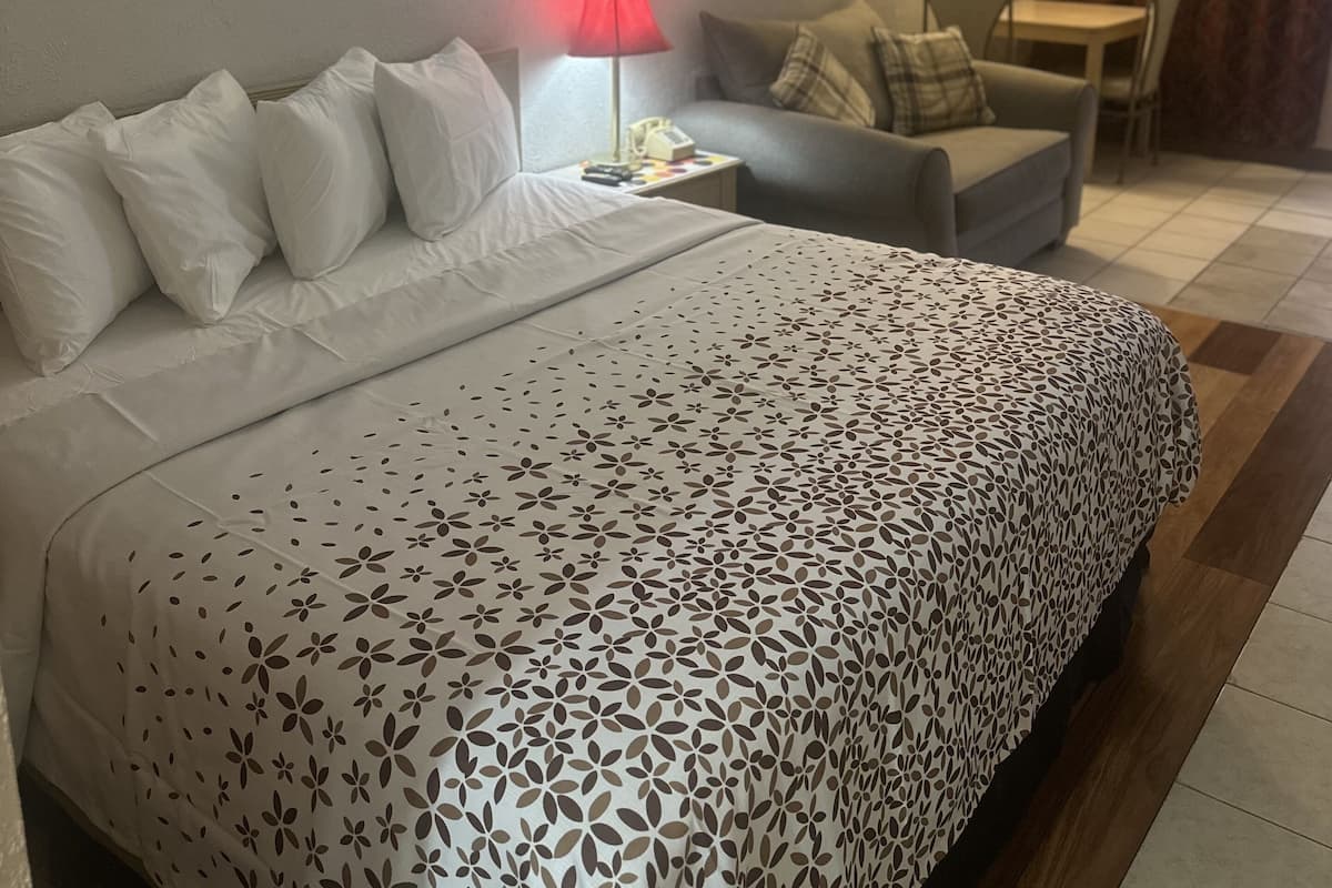 Une chambre d’hôtel avec un lit, une chaise, une petite table, une lampe et un tableau au mur.
