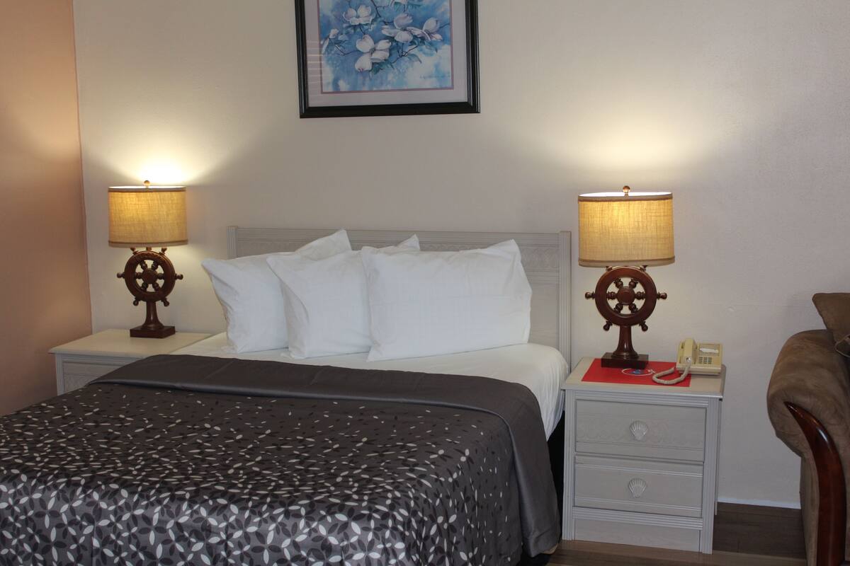 Une chambre d’hôtel comprenant un lit, deux tables de chevet avec des lampes, une petite table avec un téléphone et un tableau encadré au mur.
