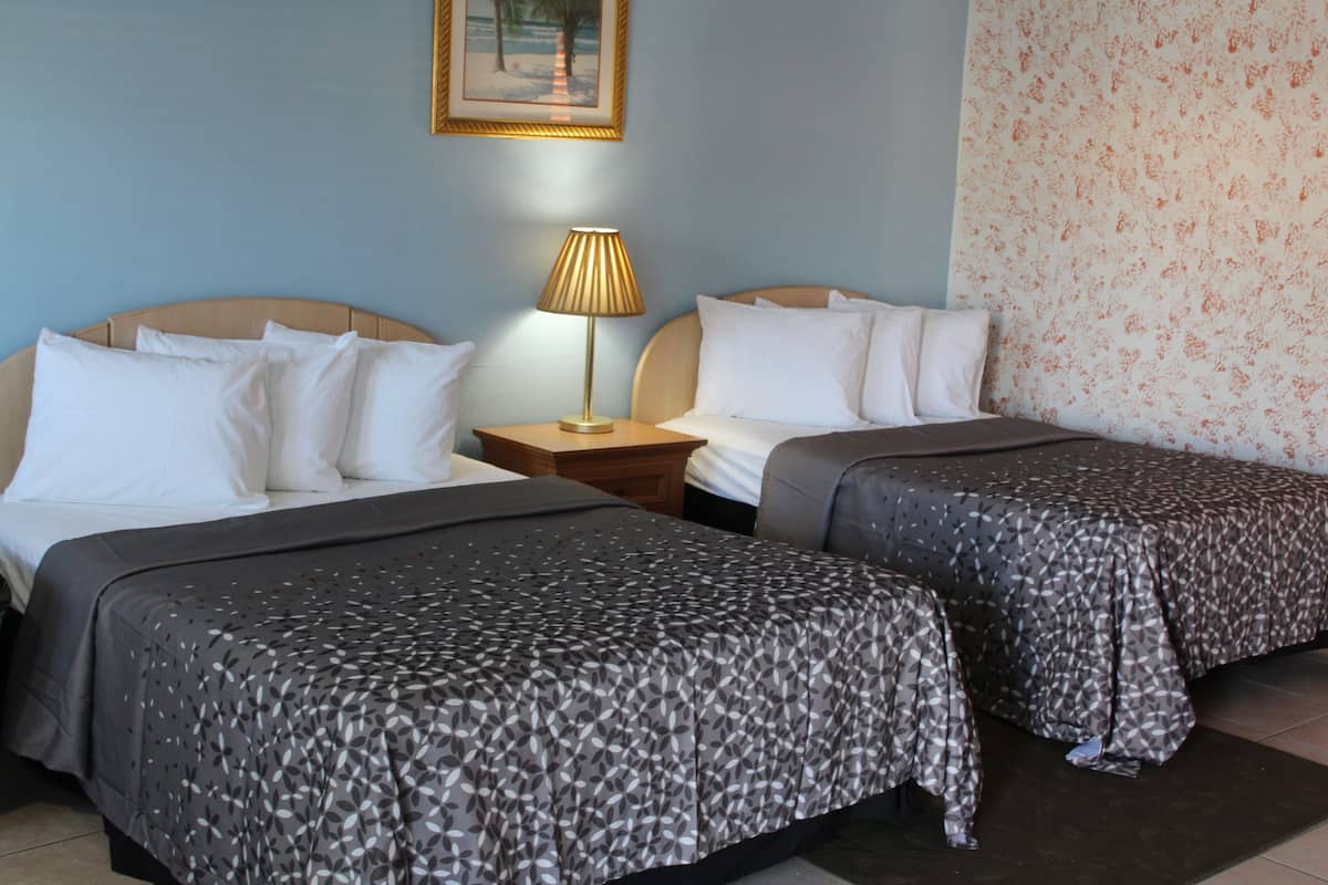 Une chambre d’hôtel avec deux lits, une table de chevet avec une lampe et un papier peint à motifs floraux sur le mur.