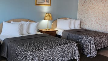 A hotel room with two beds, a nightstand with a lamp, and a floral wallpaper on the wall.