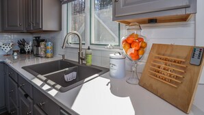 A kitchen with a sink, a window, a soap dispenser, and a wooden board with words.