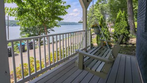 A wooden deck with a bench, overlooking a lake with a dock and boats.